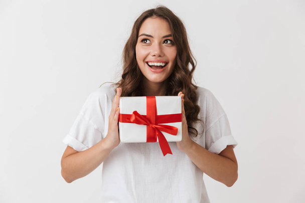 Portrait of a happy young casual brunette woman holding present box isolated over white background - Zdjęcie, obraz