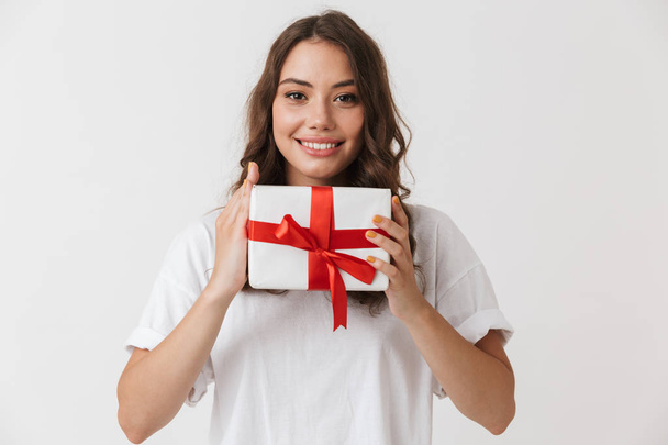 Portrait of a cheerful young casual brunette woman holding present box isolated over white background - Valokuva, kuva