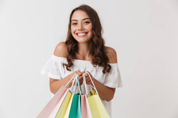 Portrait of an excited young casual brunette woman holding shopping bags isolated over white background - Fotografie, Obrázek