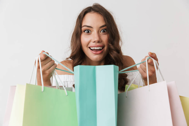 Portrait of a happy young casual brunette woman holding shopping bags isolated over white background - Foto, Bild