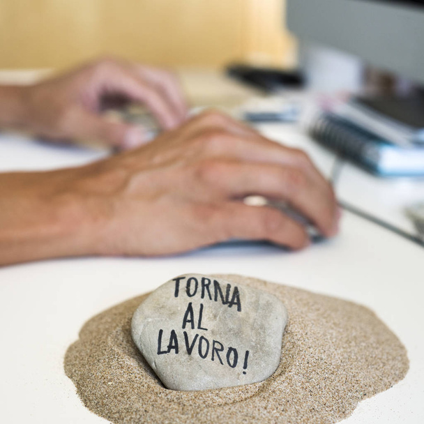 zbliżenie, człowiek siedzi na jego biurko i kamienia na stertę piasku na pierwszym planie z tekstu torna al lavoro, z powrotem do pracy pisemnej w włoski - Zdjęcie, obraz