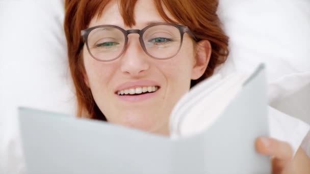 Red-haired girl reading a book in a white bed. top view - Footage, Video
