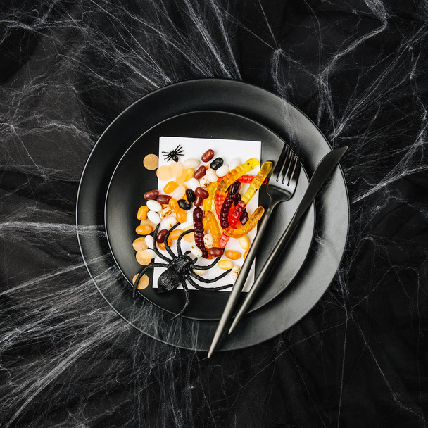 black plate with halloween sweetsand spider on dark table  - Fotografie, Obrázek