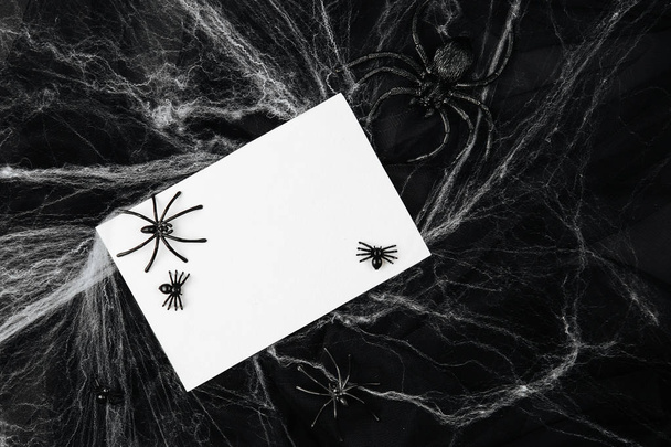 Tarjeta en blanco con arañas y tela sobre fondo negro
 - Foto, imagen