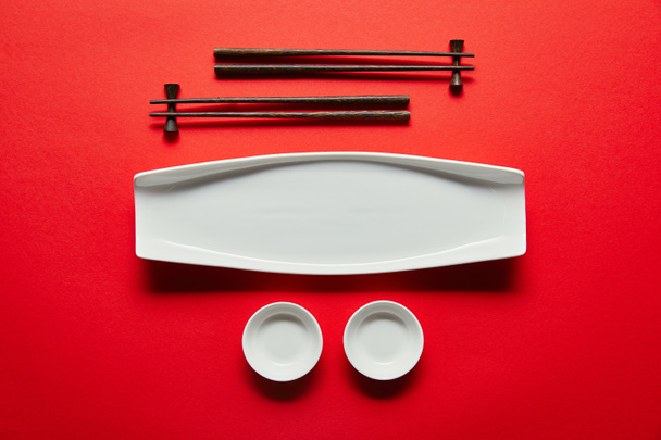 flat lay with arranged empty bowls, plate and chopsticks on red background - Zdjęcie, obraz