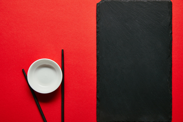 top view of arranged empty bowl, chopsticks and slate plate on red background - Fotoğraf, Görsel
