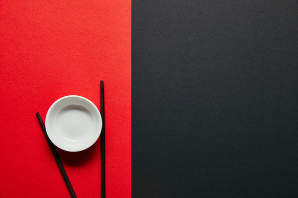 top view of arranged empty bowl and chopsticks on red and black background - Fotografie, Obrázek