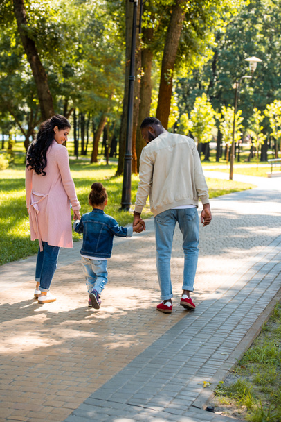 vue arrière des parents afro-américains et de leur fille se tenant la main et marchant dans le parc
 - Photo, image
