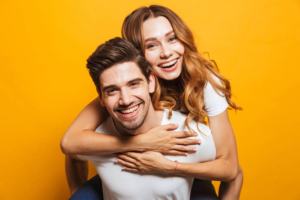 Photo of pleased adorable couple having fun while man piggybacking beautiful woman isolated over yellow background - Φωτογραφία, εικόνα