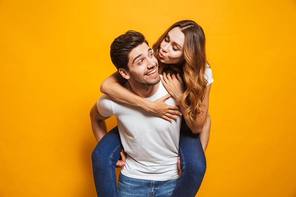 Photo of happy couple having fun while man carrying beautiful woman on his back isolated over yellow background - Foto, Imagen