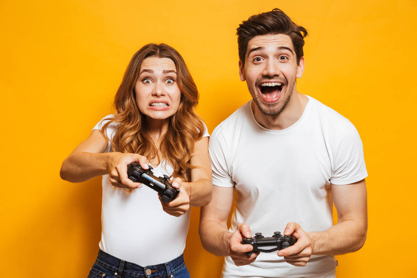 Image of joyful man and displeased woman playing together video games with joysticks isolated over yellow background - Photo, Image