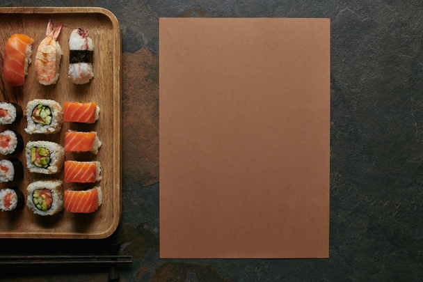 pohled shora uspořádány sushi na dřevěný talíř a hůlky na tmavý podklad - Fotografie, Obrázek