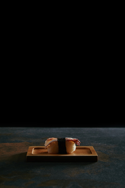крупным планом вид нигири суши с креветками на деревянной тарелке на черном фоне
 - Фото, изображение