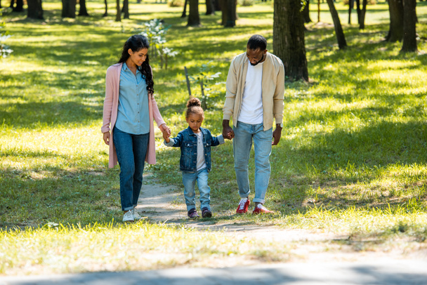 african american parents and daughter holding hands and walking in park - Foto, imagen