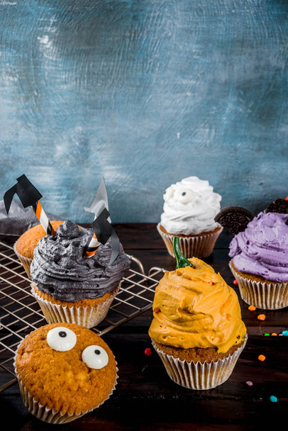 Funny children's treats for Halloween: variations of cupcakes, decorated in the form of different monsters, witches, pumpkins, ghosts. Cooking process. On a wooden table, copy space for text, top view - Fotoğraf, Görsel