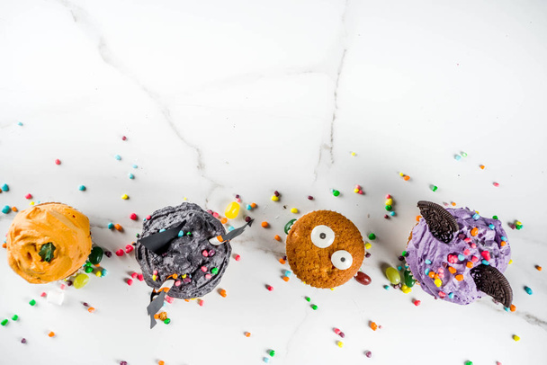 Αστεία Παίδων Απόκριες απολαύσεις: παραλλαγές των cupcakes, διακοσμημένο με τη μορφή διαφορετικά τέρατα, μάγισσες, φαντάσματα και κολοκύθες. Χώρο αντίγραφο φόντο λευκό μάρμαρο για το κείμενο, - Φωτογραφία, εικόνα