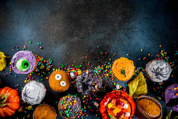 Leuke Kinder traktaties voor Halloween: variaties van cupcakes, ingericht in de vorm van verschillende monsters, heksen, pompoenen, spoken. Donkere roestig blauwe achtergrond kopie ruimte voor tekst, bovenaanzicht - Foto, afbeelding