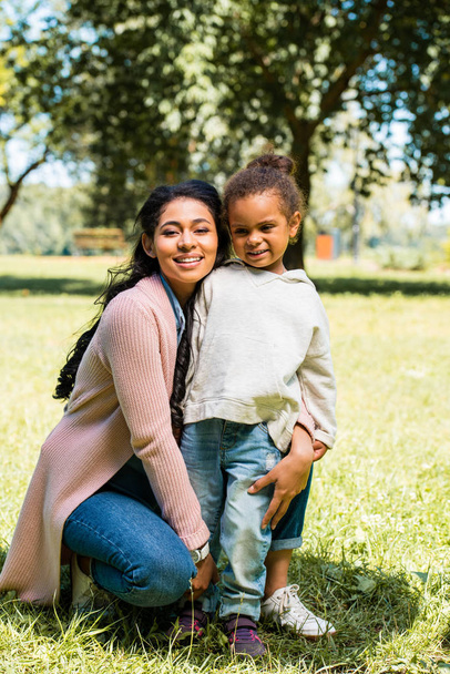mosolygó afro-amerikai anya lánya átölelve és látszó-on fényképezőgép-park - Fotó, kép