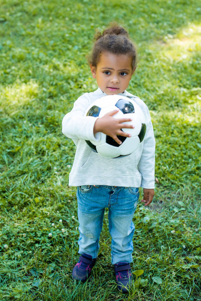 adorable african american kid holding football ball and looking away in park - Fotoğraf, Görsel