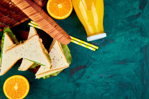 緑のテーブルの上でピクニック。赤いチェックのテーブル クロス、バスケット、健康食品サンドイッチ、フルーツ、オレンジ ジュース。夏の時間の残り。フラットを置く - 写真・画像