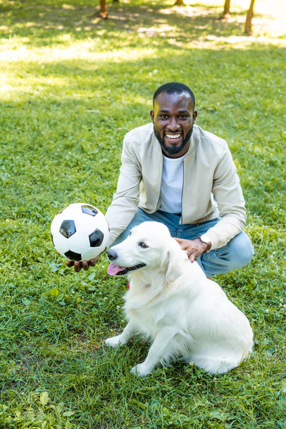csinos afroamerikai férfi, gazdaság futball-labda, és palming kutya Park - Fotó, kép