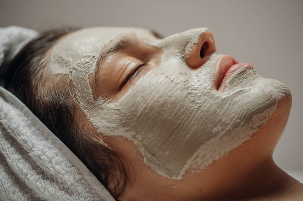 Mulher branca bonita jovem com uma máscara facial natural em seu rosto deitado na mesa de massagem
. - Foto, Imagem