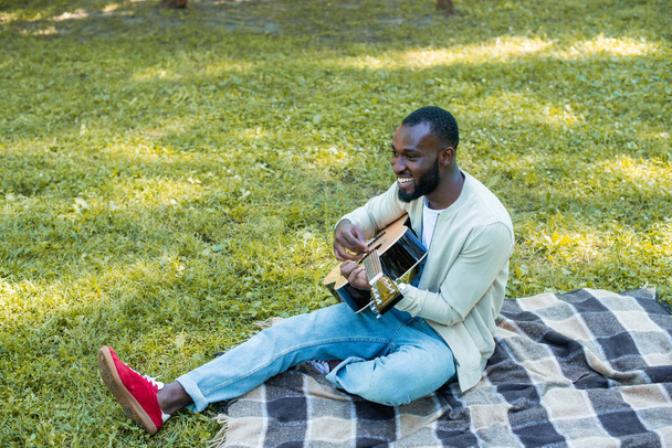 handsome african american guitarist playing acoustic guitar in park - Fotó, kép