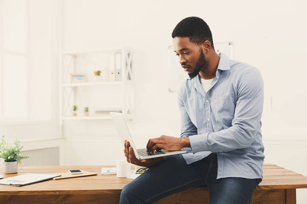 Jonge zwarte zakenman die op laptop werkt op kantoor - Foto, afbeelding