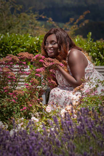 Junge kurvige Frau in einem Sommerkleid geniet den Duft der Blumen - Foto, immagini