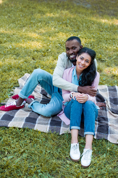 high angle view of smiling african american boyfriend hugging girlfriend in park  - Zdjęcie, obraz