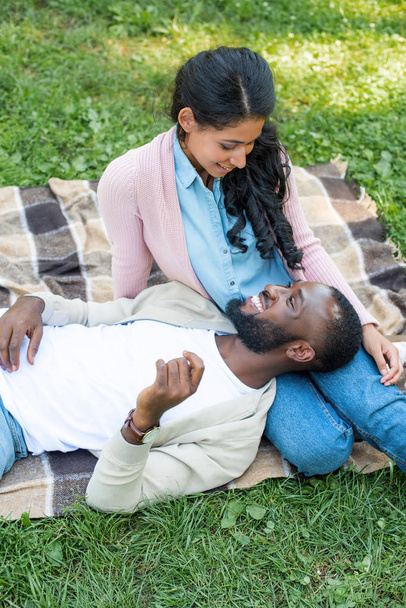 high angle view of happy african american boyfriend lying on girlfriend legs in park - Valokuva, kuva