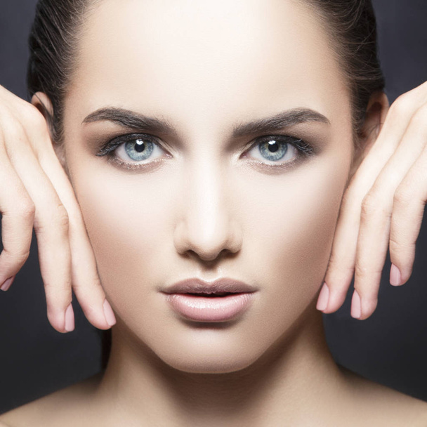 portrait of woman with natural makeup touching cheeks by hands and looking at camera  - Foto, Imagen