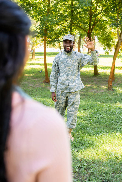 cropped image of smiling african american soldier in military uniform waving hand to girlfriend in park - Foto, imagen