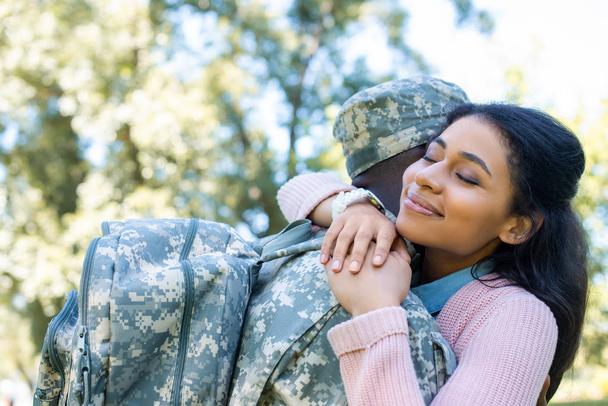 Αφρικανικός Αμερικανός στρατιώτης σε στρατιωτική στολή αγκαλιάζει φίλη στο πάρκο - Φωτογραφία, εικόνα