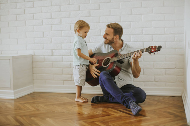 Father and little son with guitar at home - Фото, изображение