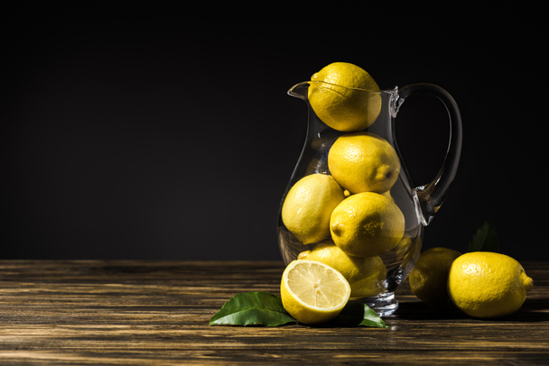 glass jug with yellow lemons on wooden tabletop - Fotó, kép