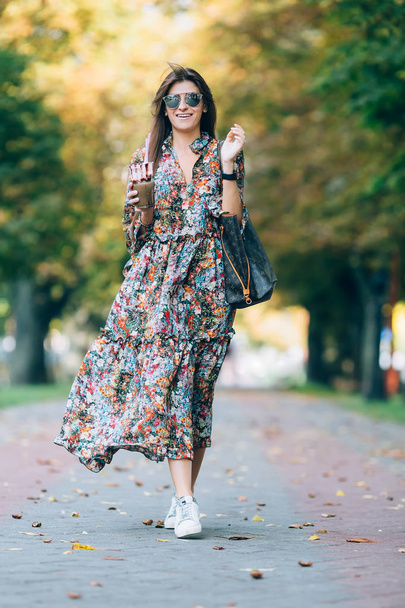 Молодая женщина в солнечных очках с молочным коктейлем. Портрет симпатичной улыбающейся женщины, гуляющей в осеннем парке
 - Фото, изображение