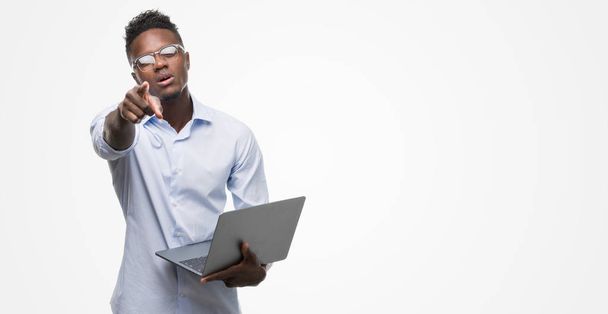 Молодой африканский американский бизнесмен, использующий компьютерный ноутбук указывая пальцем на камеру и на вас, знак руки, позитивный и уверенный жест спереди
 - Фото, изображение