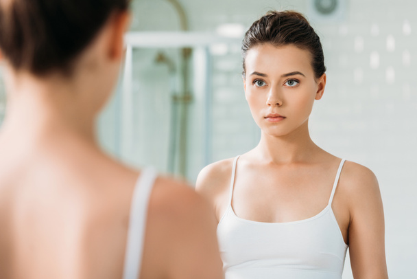 красивая молодая женщина в нижнем белье смотрит в зеркало в ванной комнате
 - Фото, изображение
