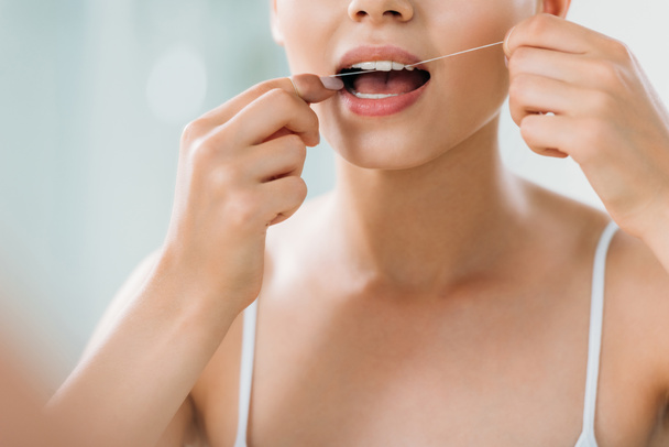 cropped shot of young woman using dental floss in bathroom - Zdjęcie, obraz