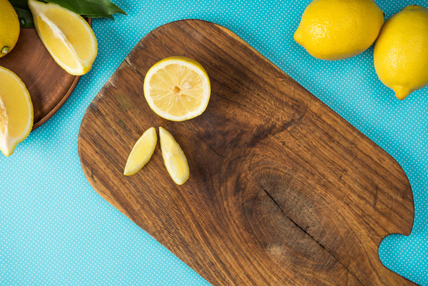 top view of fresh yellow lemons on wooden cutting board on turquoise background - Foto, Imagen
