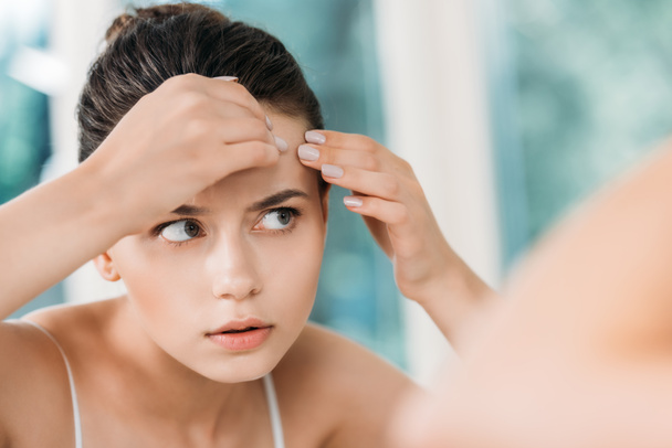 szelektív összpontosít lány bőr a homlokon, és keresi a tükör a fürdőszobában ellenőrzése   - Fotó, kép