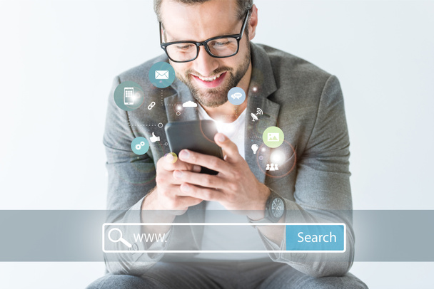 développeur de référencement souriant en costume gris à l'aide d'un smartphone, isolé sur blanc avec barre de recherche de site Web et icônes
 - Photo, image