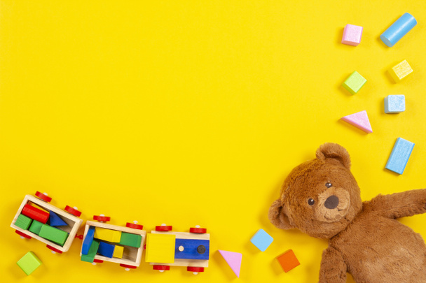 Baby kids toys background with teddy bear, wooden train, colorful blocks and bricks on yellow background. Top view - Photo, Image
