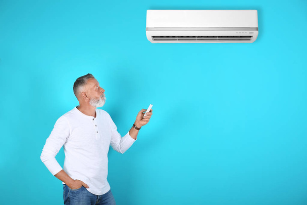 Mature man operating air conditioner on color background - Foto, Imagem