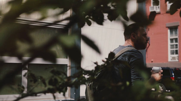 Счастливый успешный красивый европейский мужчина с рюкзаком прогуливаясь по тенистому лету Нью-Йорк-стрит пить кофе
. - Кадры, видео