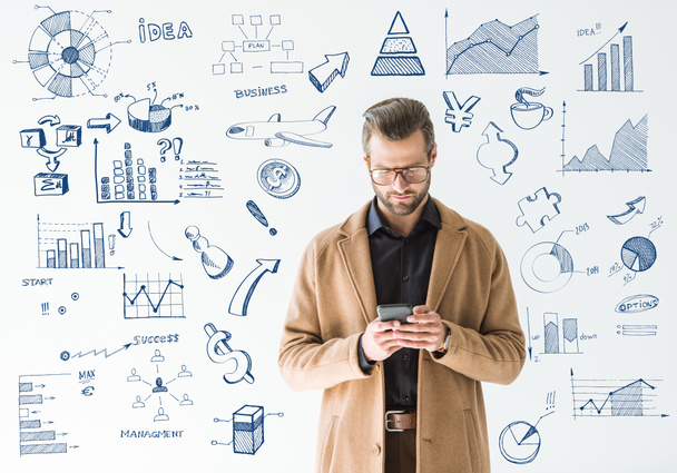 handsome developer in brown coat using smartphone, isolated on white with SEO and business icons - Photo, Image