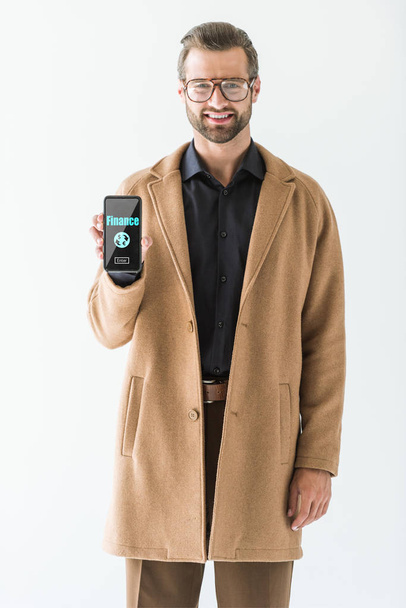 Lächelnder Geschäftsmann präsentiert Smartphone mit Finanz-Ikone auf Bildschirm, isoliert auf Weiß - Foto, Bild