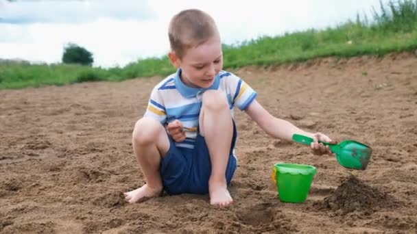 Kisfiú játszik ástak gödröt, egy lapáttal. Gyerek játszik a tengerparton - Felvétel, videó