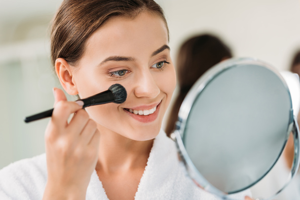 close-up view of beautiful brunette girl applying makeup and looking at mirror  - Fotó, kép